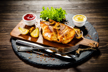 Grilled chicken fillet and vegetables served on black stone on wooden table