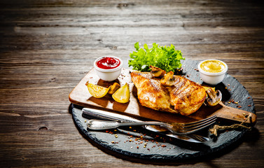 Grilled chicken fillet and vegetables served on black stone on wooden table