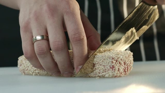 Chef knife cut the tuna fillet into two halves on the white Board. Slow motion filming close-up