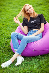 Fototapeta premium Girl sitting on grass in park on chair bag
