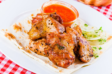 Grilled pork with tomato sauce, onion and pita bread on white plate