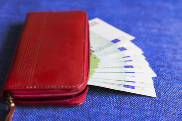 red wallet with Euro banknotes, on blue background