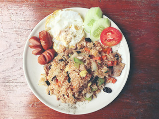 American style breakfast set, fried rice and the style fried egg and sausage in white dish  on wooden table. Thai food. vintage tone color.