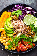 Buddha bowl dish with brown rice, avocado, pepper, tomato, cucumber, red cabbage, chickpea, fresh lettuce salad and walnuts. Healthy vegetarian eating, super food. Top view