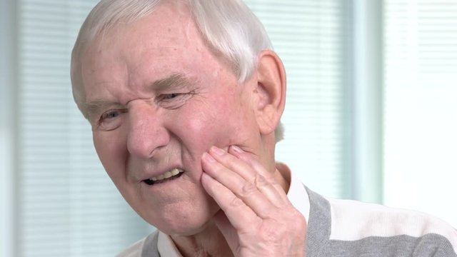 Unhappy senior man having toothache. Stressed elderly man with terrible toothache on blurred background close up.