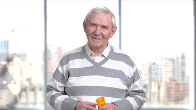 Elderly man with a bottle of pills. Pensioner holding container with medicine and looking at camera. Blood pressure has increased.