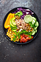 Buddha bowl dish with brown rice, avocado, pepper, tomato, cucumber, red cabbage, chickpea, fresh lettuce salad and walnuts. Healthy vegetarian eating, super food. Top view