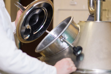 Person wearing white lab coat opening a reservoir for inspection, beer production close up