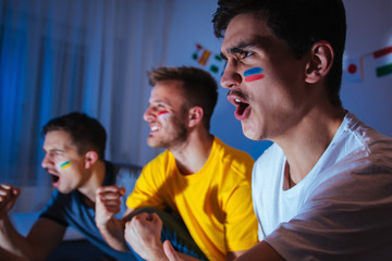 Young men watching football match at home, exited and focused on the game, celebrating and shouting