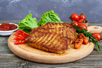 Juicy steaks with greens and vegetables on a wooden tray. A large piece of pork tenderloin grilled.