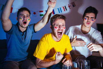 Young men watching football match at home, exited and focused on the game, celebrating and shouting 