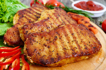 Juicy steaks with greens and vegetables on a wooden tray. A large piece of pork tenderloin grilled.