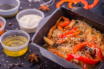 The Chinese noodles with fried mushrooms, fried red pepper on a grill, with sauce and sesame