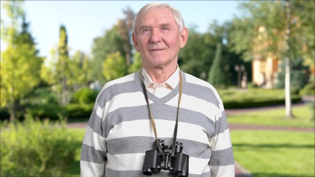 Caucasian pensioner with binoculars outdoors. Elderly man with binoculars round neck on nature background. Searching for adventure.