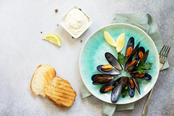 Mussels boiled in a sauce of white wine, served with toast, garlic sauce and lemon. Gourmet italian cuisine. Flat lay. Top view.