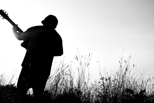 Abstract beautiful man playing Guitar in the foreground on clear sky background.