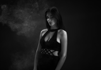Beautiful girl in a black dress in the smoke. Dark background.