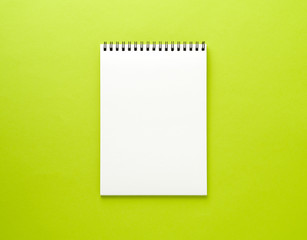 Blank notepad white page on green desk, color background. Top view,  empty space for text.