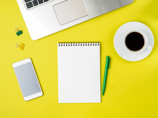 Top view of modern bright yellow office desktop with blank notepad, computer, smartphone. Mock up, empty space