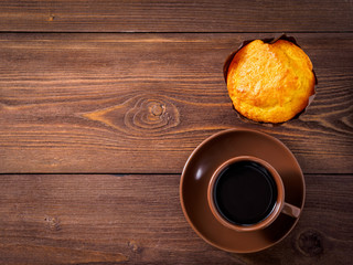 hot coffee in a Cup on a saucer, sweet tasty muffin, on brown wooden background, copy space, top view