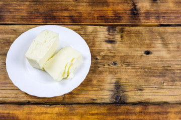 Fresh farm piece of butter on a white plate on wooden background. Farm products. Top view.