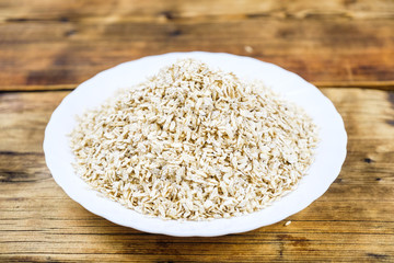 Close-up dry oat flakes in white plate in a wood background. Farm-fresh product. Top view.