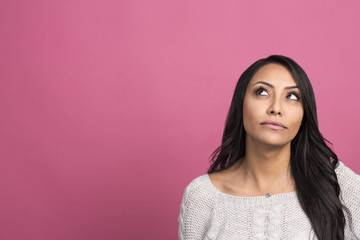 Fototapeta premium portrait of thoughtful young woman dressed in white sweater posing over pink background and looking aside to copyspace