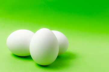 Three chicken eggs on a bright green background.