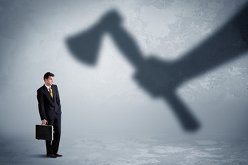 Fototapeta premium Businessman afraid of a huge shadow hand holding an axe concept