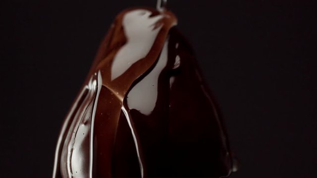 strawbery on black, covered by chocolate. Macro of chocolate texture and drop of syrup pouring on it