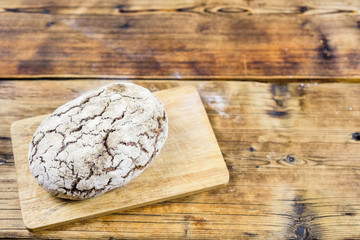 Homemade fresh rye bread on board on wooden background. Left on photo. Top view