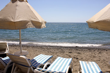 umbrellas and striped sun loungers on a sunny afternoon on a sandy beach by the blue sea without...