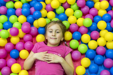Fototapeta na wymiar Cute and pretty little girl looking at camera inside heap of multi-colored balloons