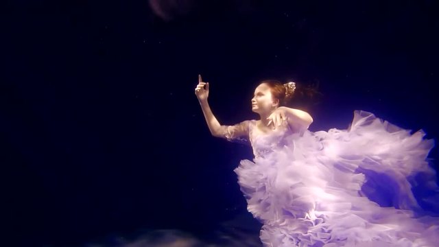 a young girl in a gorgeous dress is dancing or floating under the water, a fairy picture in the sea
