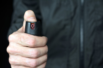 pepper gas in the hand of a young man in a black jacket CS spray self-defense Tear gas concept, close up, selective focus , blurred dark background