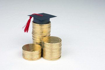 graduation mortarboard and golden coins on white background, education concept close up, selective focus