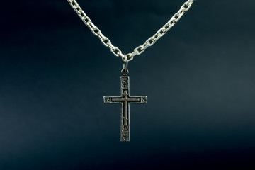 christian cross on a silver chain, faith, spirituality and religion concept. selective focus, dark blurred  background