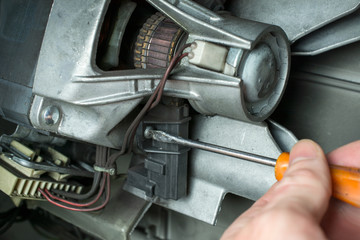 Fototapeta premium hand of a repairman with a screwdriver repair of the electric motor of the washing machine, replacement of brushes, home appliances repair & services concept