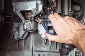 repairer hand with pliers fix the electric motor of the washing machine, replacement of brushes,...