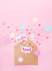 Multicolor sweets sugar candy hearts, handcraft paper flowers and cards with Hello April lettering fly out of craft paper envelope on pink background . Spring concept. Space for text. Vertical format.
