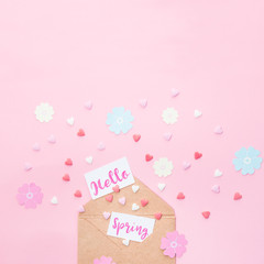 Multicolor sweets sugar candy hearts, handcraft paper flowers and cards with Hello Spring lettering fly out of craft paper envelope on pink background . Art concept. Space for text. Square format.