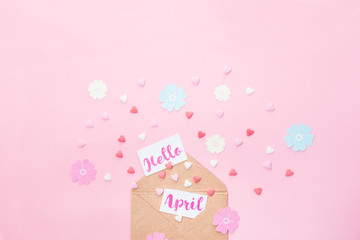 Multicolor sweets sugar candy hearts, handcraft paper flowers and cards with Hello April lettering fly out of craft paper envelope on pink background . Spring concept. Space for text. Horizontal.