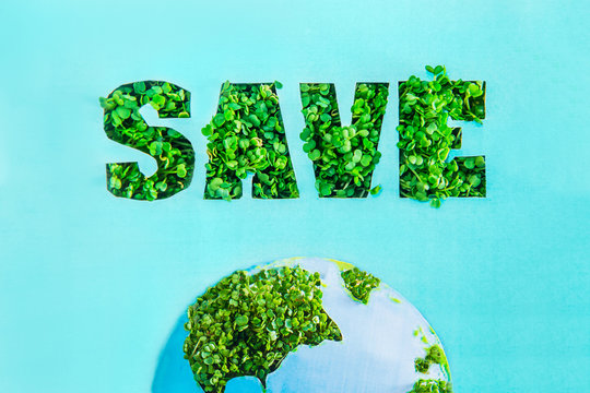 Creative concept with outline lettering Save in green fresh grass sprouts and part of planet model on blue turquoise background. Save Earth, nature. Earth Day, April 22. Space for text.