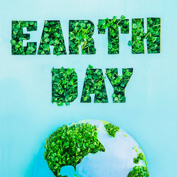 Creative concept with outline lettering Earth Day in green fresh grass sprouts and part of planet model on blue background. Save planet, nature. Earth Day, April 22. Space for text. Square.