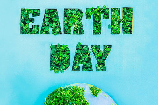 Creative concept with outline lettering Earth Day in green fresh grass sprouts and part of planet model on blue background. Save planet, nature. Earth Day, April 22. Space for text. Horizontal.