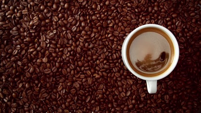 top view of hand with cup of black coffe put it on coffe beans background. White cup of black coffee