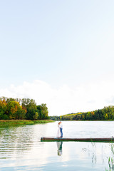 Fototapeta premium The boyfriend hugs his girlfriend standing on the pier on the ba