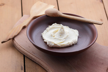 Sour cream on a clay plate on a wooden table, cream on a plate, milk dessert with a wooden spoon, vegan, simple food, retro style milk pattern, rustic style, dairy product, copy space