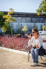 A woman speaks by mobile phone while sitting on a bench in a park