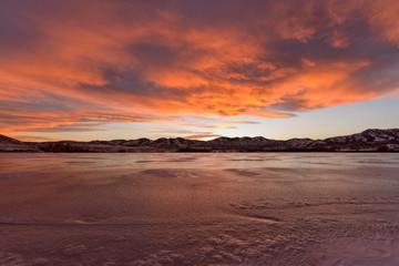 Fototapeta na wymiar Fiery Clouds - bright and colorful winter sunset clouds rolling over a frozen mountain lake.